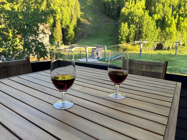 Two wine glasses on a wooden table with a view of a forested area.
