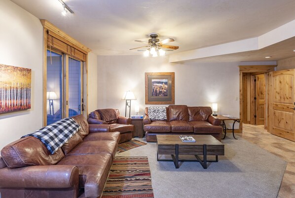 A living room with leather sofas, a wooden coffee table, and a ceiling fan.