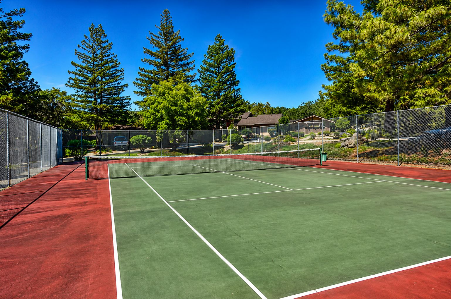A tennis court with a net, surrounded by trees and a fence.