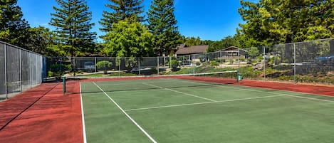 A tennis court with a net, surrounded by trees and a fence.