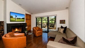 A living room with a fireplace, leather armchair, sofa, and a television mounted on the wall. - Charming Napa condo with 3 beds, garden view at Silverado (Napa)