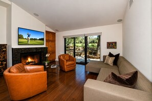 A living room with a fireplace, leather sofas, a television, and a view of a landscaped outdoor area.