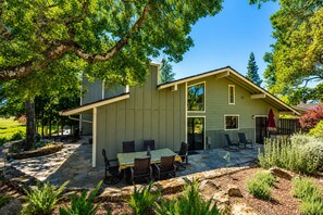 A modern house with a patio area featuring a table and chairs, surrounded by a stone pathway and greenery.