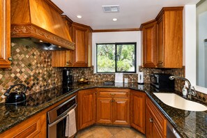 Cocina con armarios de madera, encimera de granito, ventana y horno empotrado.