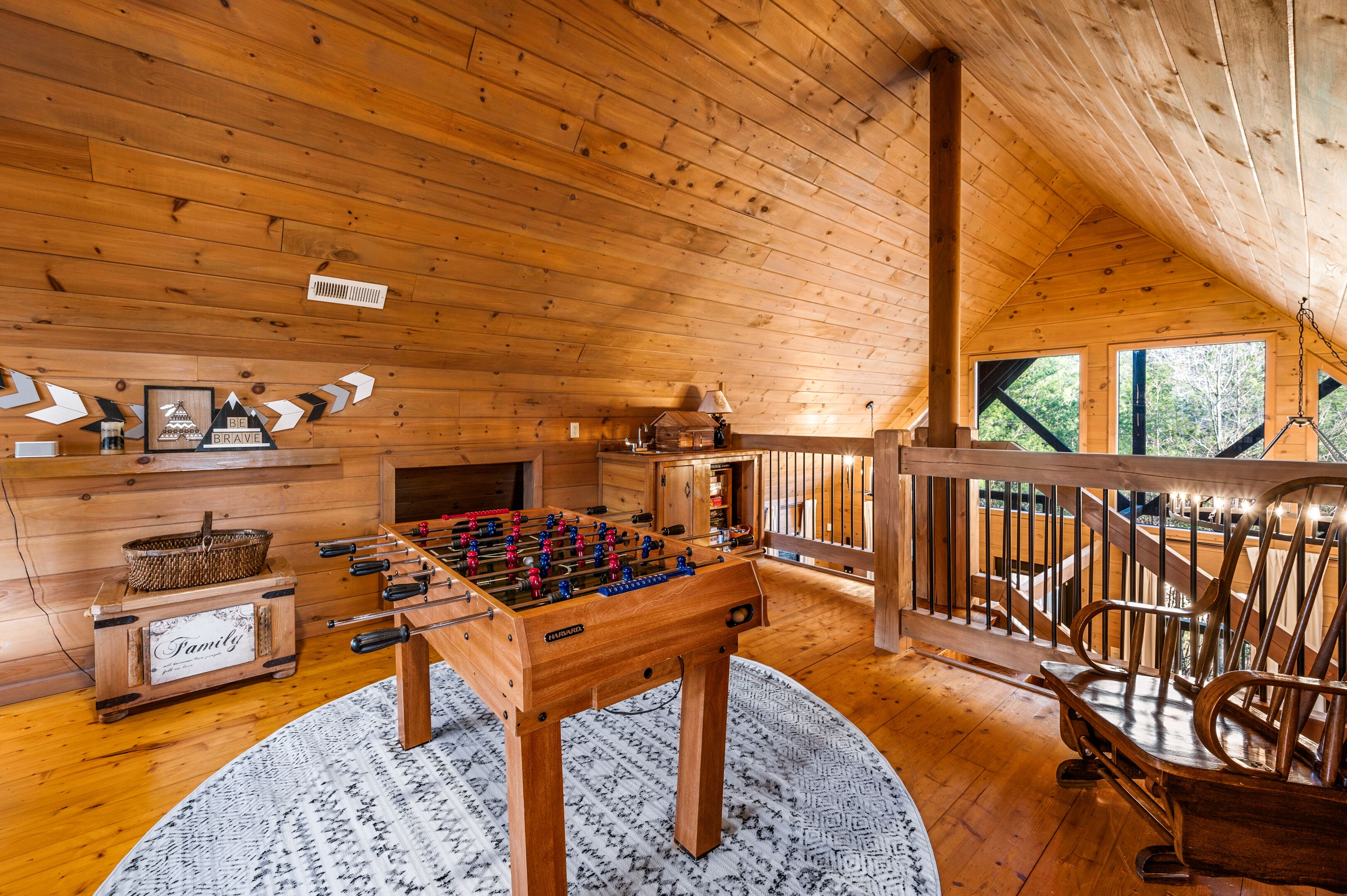 A cozy wooden cabin interior with a foosball table, a fireplace, and a rustic wooden chair.