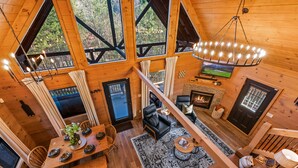 Interior de una cabaña de madera con comedor, sala de estar, chimenea y ventanas amplias.