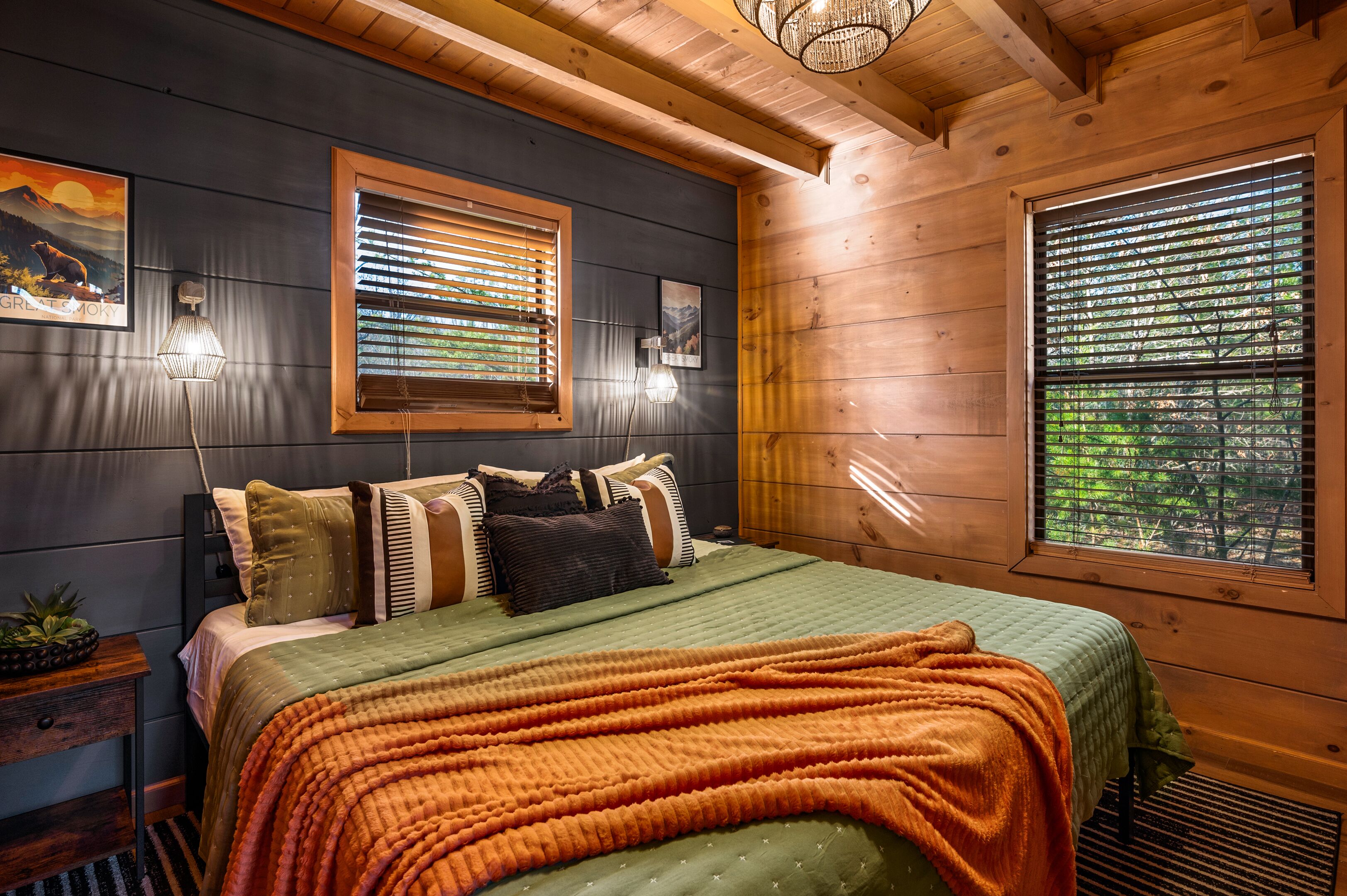 Ein gemütliches Schlafzimmer mit Bett, Kissen, einem Nachttisch, einer Lampe und zwei Fenstern mit Jalousien.