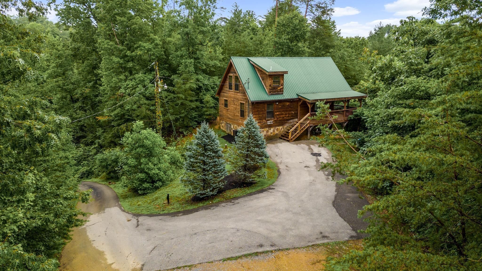 A log cabin with a green roof, surrounded by dense forest.