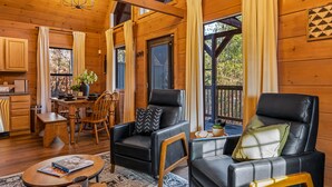 Interior acogedor de una cabaña con paredes de madera, una zona de comedor, dos sillones de cuero, una mesa de centro y un ventanal con cortinas.