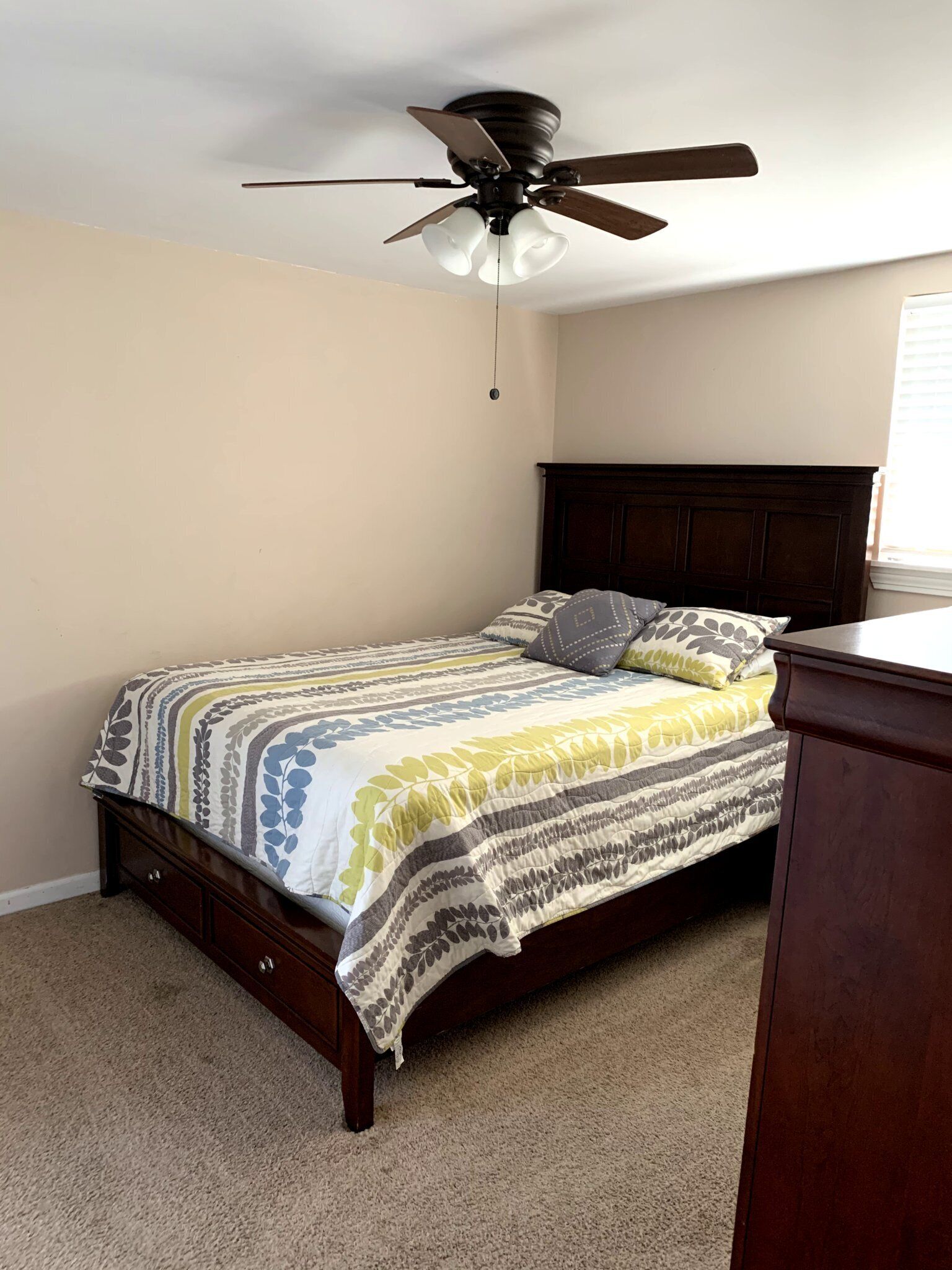 A bedroom with a single bed, a wooden headboard, a ceiling fan, and a window with blinds.