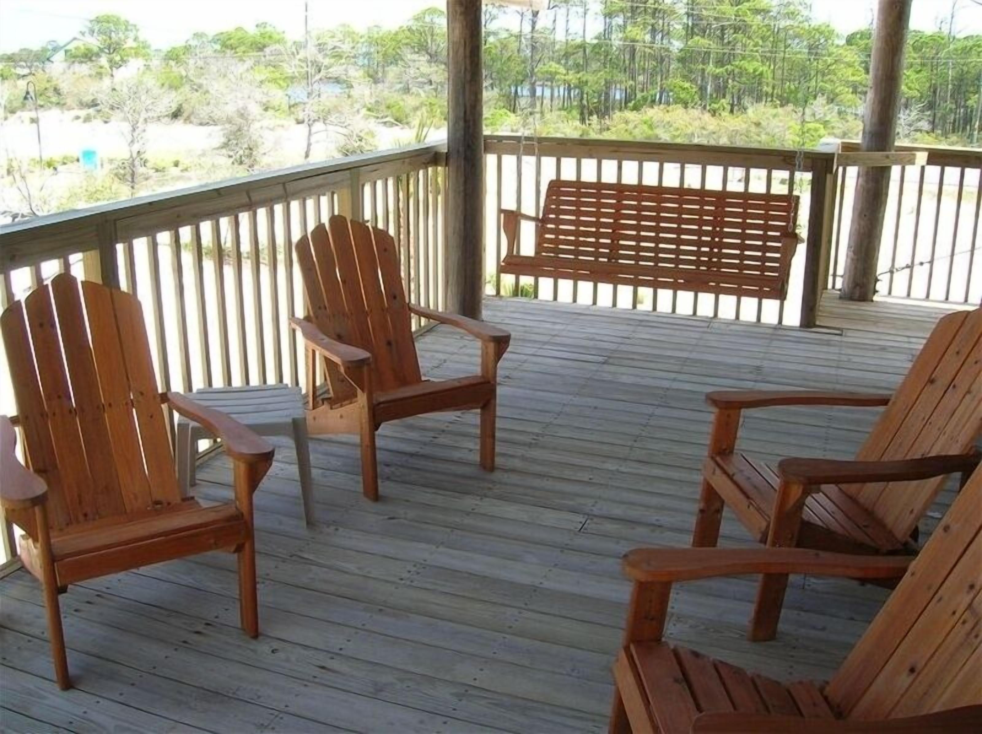 Une terrasse en bois avec quatre chaises Adirondack et un banc en bois.