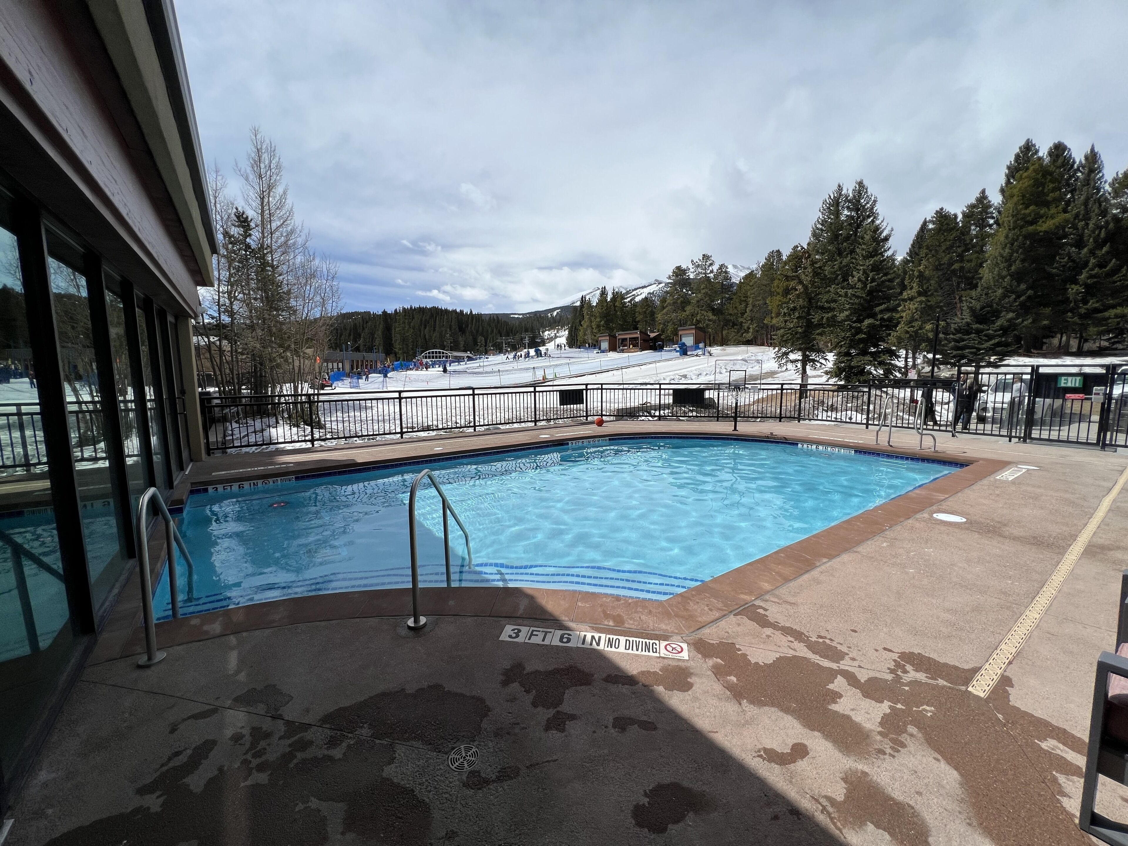 A swimming pool with a 3 ft depth limit sign, surrounded by a concrete deck and a metal fence.