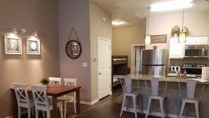 Una cocina moderna con electrodomésticos de acero inoxidable, un comedor con mesa de madera y sillas blancas, y un pasillo que conduce a un dormitorio.