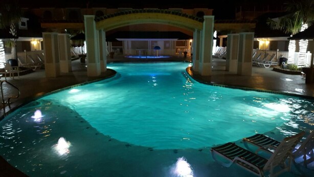 Una piscina con un arco central, rodeada de sillas de descanso y una zona bien iluminada.
