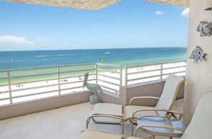 Un balcón con vista a la playa, una silla y una mesita.