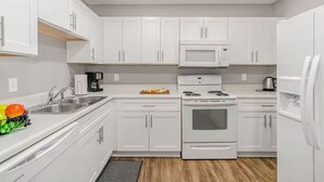 Una cocina moderna con gabinetes blancos, un lavamanos de acero inoxidable, un microondas, una estufa y un refrigerador.