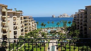 A resort with multiple buildings, a swimming pool, and a view of the ocean with rocky formations in the distance. - UNBELIEVABLE VIEWS-EXTRA LARGE BALCONY FOUR LOUNGE CHAIRS 3 KING BEDS (Cabo San Lucas)