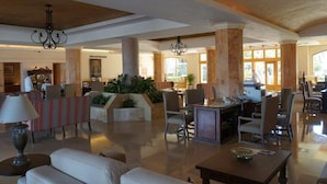 A spacious lobby with high ceilings, large columns, and a chandelier. There are seating areas with tables and chairs, and a reception desk with a computer and phone. - UNBELIEVABLE VIEWS-EXTRA LARGE BALCONY FOUR LOUNGE CHAIRS 3 KING BEDS (Cabo San Lucas)