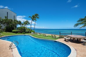 A swimming pool with a view of the ocean, surrounded by palm trees and a building.