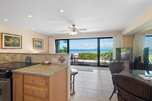 A kitchen with a view of the ocean, a dining area with a TV, and a ceiling fan.