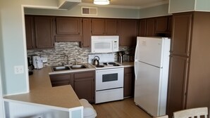 Une cuisine de taille réduite avec des meubles de couleur marron, un micro-ondes blanc, une cuisinière et un réfrigérateur.