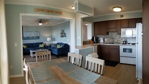 Un salon avec un canapé bleu, une table basse et une table à manger avec des chaises. Il y a également un coin cuisine équipé d’un four à micro-ondes, d’une cuisinière et de placards.