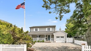 A two-story house with a front porch, a garage, and a flagpole with an American flag. - Newly renovated upscale Beach House  (Bay Head)