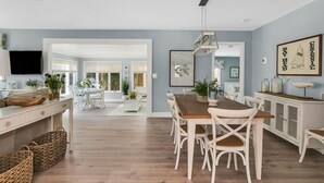 A spacious kitchen with a wooden dining table, white chairs, and a hanging light fixture. - Newly renovated upscale Beach House  (Bay Head)