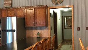 A kitchen with wooden cabinets, a stainless steel refrigerator, and a wooden dining area with chairs. - Adirondacks Family Retreat (Fort Ann)