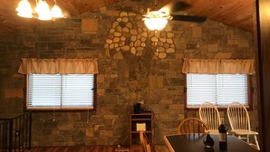 A dining area with a stone wall, wooden ceiling, and two windows with curtains. - Adirondacks Family Retreat (Fort Ann)