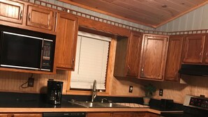 A kitchen with wooden cabinets, a stainless steel dishwasher, a microwave, a sink, and an oven. - Adirondacks Family Retreat (Fort Ann)