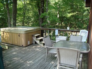 Um deck de madeira com uma banheira de hidromassagem, móveis de exterior e vista para uma área arborizada.