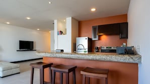 A modern kitchen with granite countertops, a built-in oven, and a coffee maker. There are three wooden stools in front of the counter.
