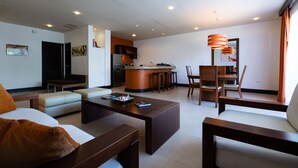A modern living room with a sofa, coffee table, and dining area with chairs and a kitchen in the background.