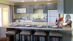 Una cocina con armarios grises, una isla central con taburetes de bar, un microondas, un refrigerador y una cafetera.