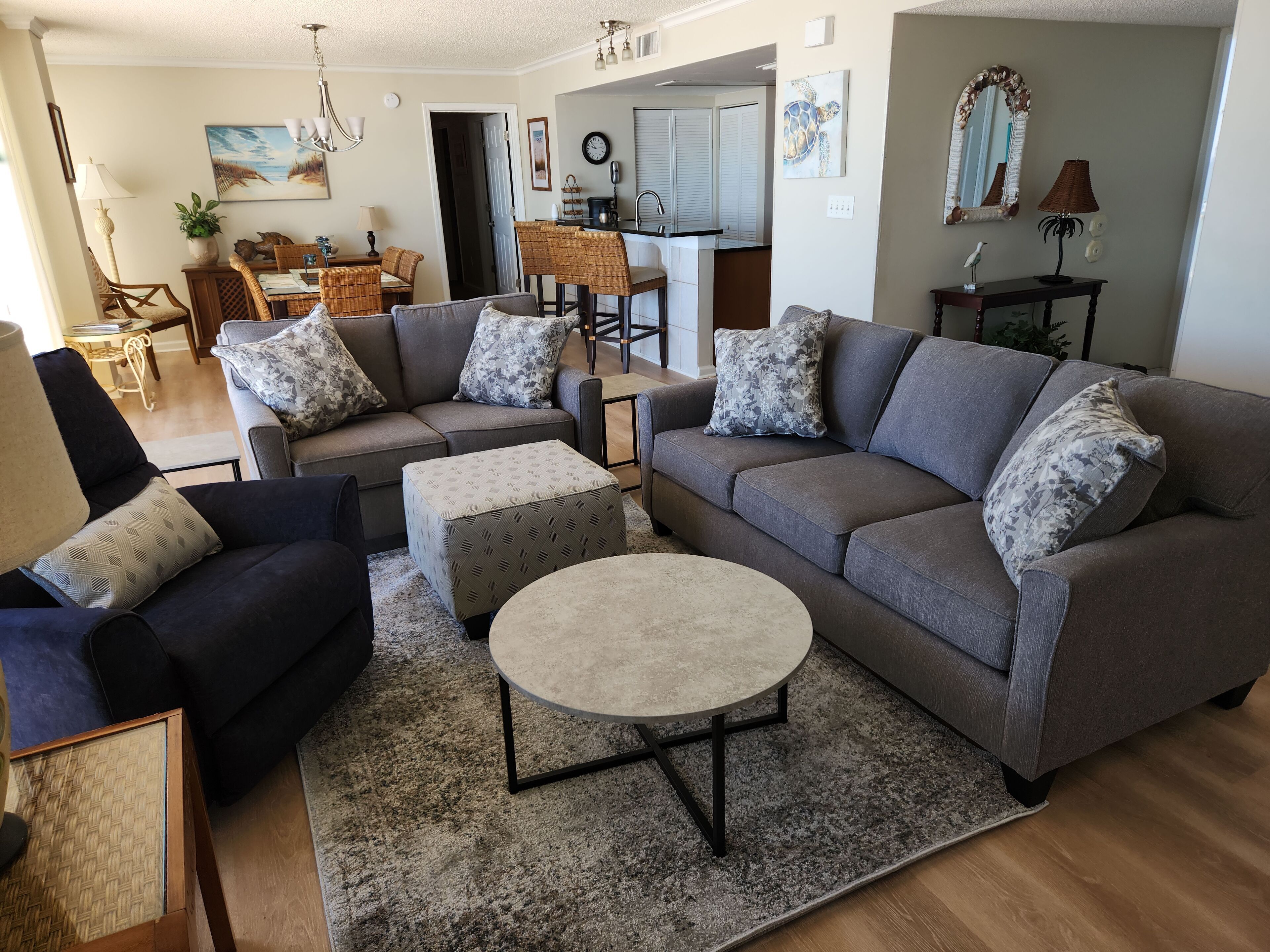 Ein Wohnzimmer mit grauem Sofa, einem runden Couchtisch und einem Essbereich im Hintergrund.