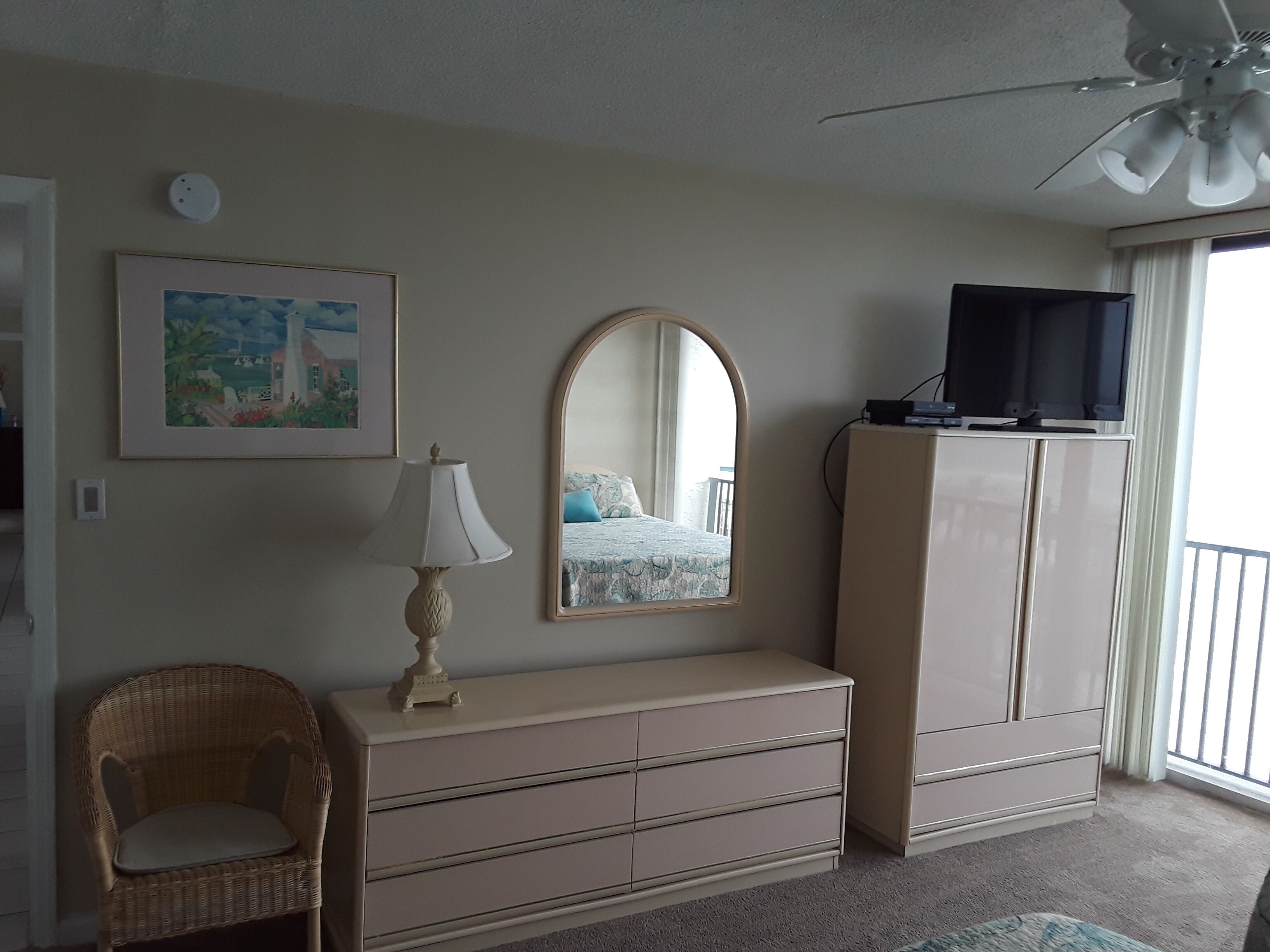 A bedroom with a bed, dresser, television, and a ceiling fan.