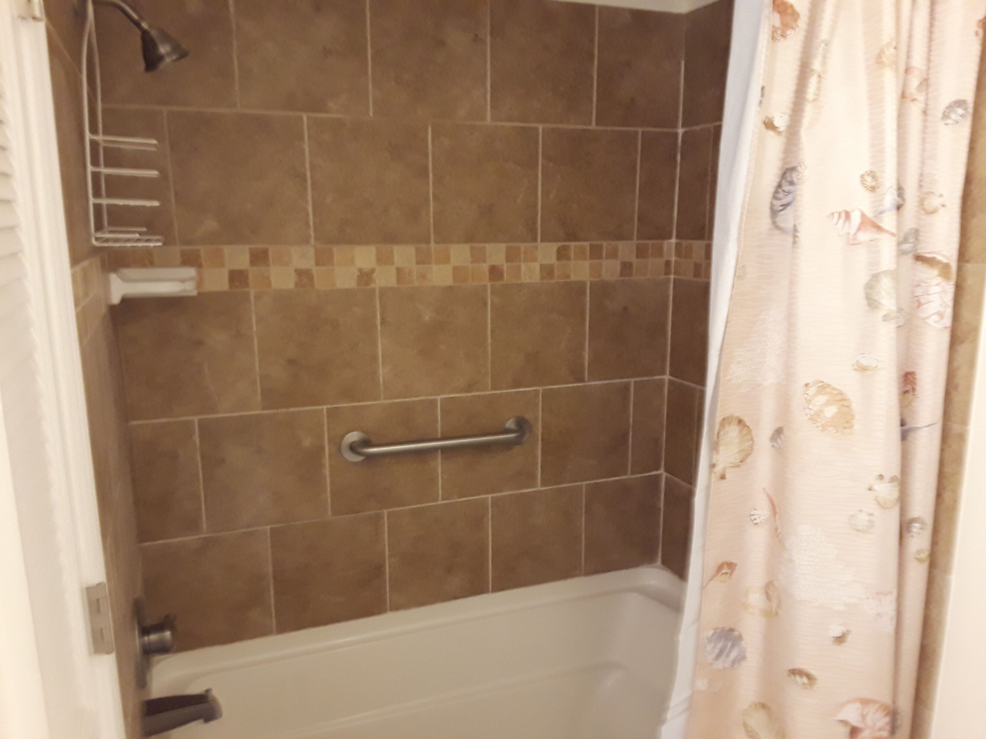 Une salle de bain avec une douche, des murs carrelés, une barre d’appui et un rideau à motifs floraux.