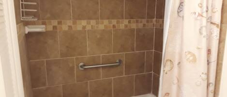 Une salle de bain avec une douche, des murs carrelés, une barre d’appui et un rideau à motifs floraux.