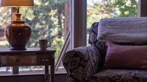 Una habitación con un sillón estampado, una lámpara y una taza sobre una mesita.