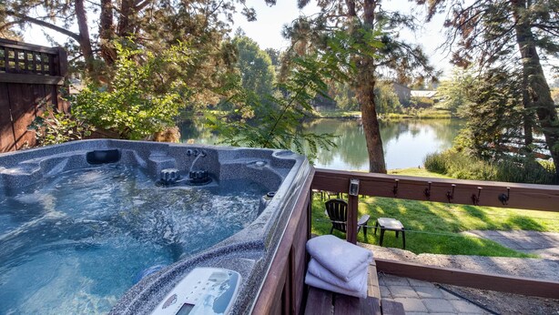 Un jacuzzi con terraza de madera y vista a un lago rodeado de árboles.