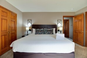 A large bed with a dark headboard, two bedside lamps, and a pair of decorative pillows.