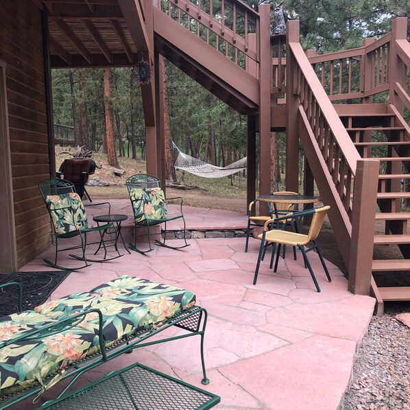 A covered patio with outdoor furniture, a hammock, and a wooden staircase.