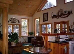 Cozy cabin-style interior with a rustic aesthetic, featuring a wooden ceiling, large window, and comfortable seating area.