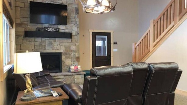 A living room with a stone fireplace, leather sofa, and a television mounted on the wall. - Deer Creek Cabin Hot Tub, BBQ Grill, Fire Pit, 20 min Yellowstone (Island Park)