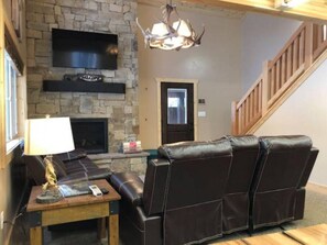 Una sala de estar con chimenea de piedra, sofá de cuero y televisor montado en la pared.