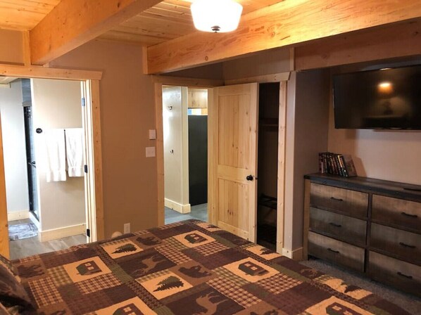 Un dormitorio con techo de madera, un televisor en la pared, un aparador y una alfombra estampada.