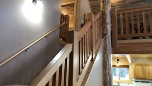 A wooden staircase with a railing, leading to a second-floor area with a kitchen visible. - Deer Creek Cabin Hot Tub, BBQ Grill, Fire Pit, 20 min Yellowstone (Island Park)