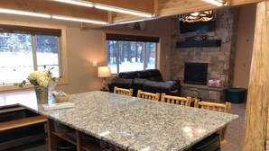A kitchen with a granite island, wooden chairs, a stone fireplace, and a view of the outdoors. - Deer Creek Cabin Hot Tub, BBQ Grill, Fire Pit, 20 min Yellowstone (Island Park)