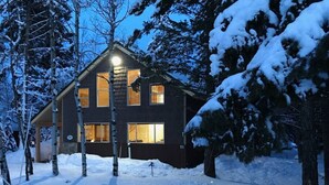 A two-story house with a dark exterior, surrounded by snow-covered trees. - Deer Creek Cabin Hot Tub, BBQ Grill, Fire Pit, 20 min Yellowstone (Island Park)